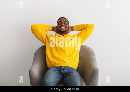 Black Guy seduto con le mani dietro la testa in poltrona indoor Foto Stock