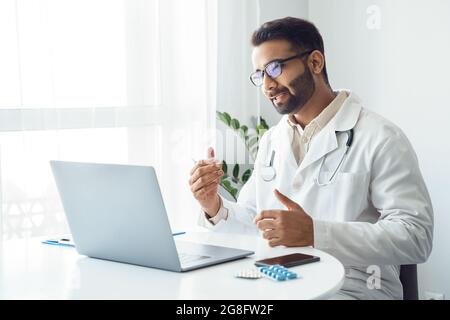 Ritratto del medico indiano che parla con il paziente online sullo schermo del computer portatile Foto Stock