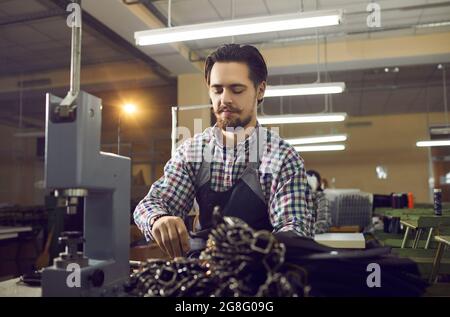 Un giovane esperto artigiano si occupa della lavorazione delle cinture in pelle sul posto di lavoro. Foto Stock