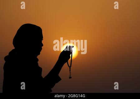 Silhouette di una donna musulmana che tiene in mano perline di preghiera e prega al tramonto, Emirati Arabi Uniti, Medio Oriente Foto Stock