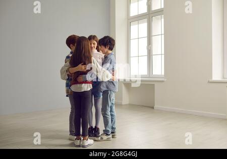 Un piccolo gruppo di bambini che si accoccolano in piedi insieme in una spaziosa camera vuota Foto Stock