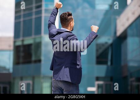 Vista posteriore di uomo d'affari in tuta formale che solleva pugni Foto Stock