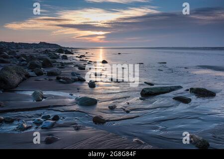 Tramonto sulla costa di Solway Firth, con riflessi sulla sabbia e sulle rocce durante una marea in arrivo. Vicino ad Allonby, Cumbria nord-occidentale, Inghilterra Foto Stock