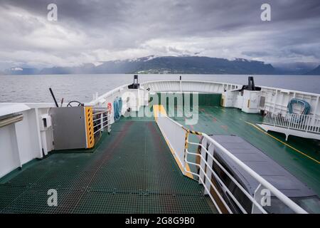 Ponte di un traghetto che naviga attraverso il fiordo norvegese in una giornata nuvolosa e piovosa con le montagne in lontananza all'orizzonte. Viaggiare in una giornata brutta Foto Stock