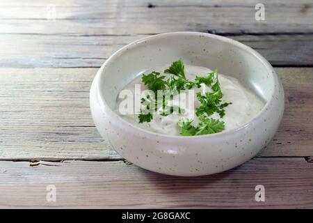 Yogurt immergere con erbe e prezzemolo guarnire in una piccola ciotola di ceramica su un tavolo di legno rustico leggero, spazio copia, fuoco selezionato, profondità di campo stretta Foto Stock