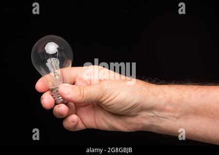 Lampadina a incandescenza nella mano di un adulto su sfondo nero. Lampadina a LED, candela di cera e lampadina di vetro. Foto Stock