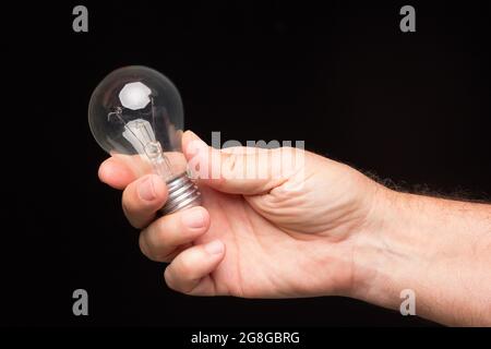 Lampadina a incandescenza nella mano di un adulto su sfondo nero. Lampadina a LED, candela di cera e lampadina di vetro. Foto Stock