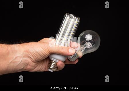 Lampadina a incandescenza nella mano di un adulto su sfondo nero. Lampadina a LED, candela di cera e lampadina di vetro. Foto Stock