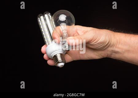 Lampadina a incandescenza nella mano di un adulto su sfondo nero. Lampadina a LED, candela di cera e lampadina di vetro. Foto Stock