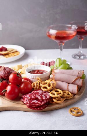 Primo piano di salumi rotondi con vari spuntini e due bicchieri con liquore rosso su sfondo grigio. Foto Stock