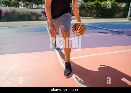 Gambe di un giocatore di basket professionista che dribbling la palla sul campo di pallacanestro. In estate durante il giorno caldo Foto Stock