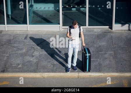 Uomo che utilizza l'app mobile nello smartphone. Passeggero con suitcace in attesa sulla strada della città. Foto Stock