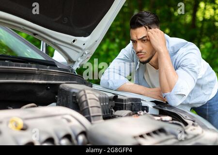 Uomo arabo perplesso appoggiato sul cofano dell'auto aperto Foto Stock