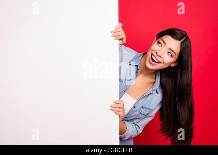 Ritratto di attraente ragazza curiosa allegra tenendo grande poster bianco ad promo isolato su sfondo rosso brillante Foto Stock