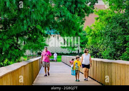 Una famiglia gioca a Pokemon Go mentre attraversa il ponte pedonale di Langan Park durante il Pokemon Go Fest 2021, 17 luglio 2021, a Mobile, Alabama. Foto Stock