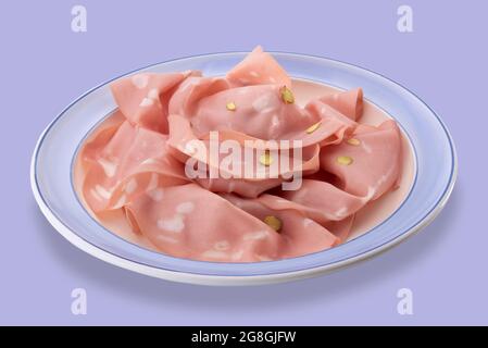 Mortadella bolognese con pistacchio, fette di salsiccia tipica italiana in piatto con bordo blu isolato su blu Foto Stock