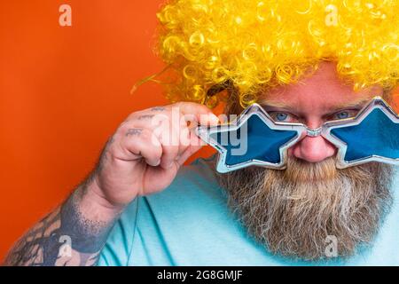 Uomo grasso premuroso con barba, tatuaggi e occhiali da sole ha dubbi su qualcosa Foto Stock