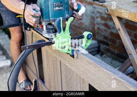 Lavora densamente con una fresatrice sulla superficie in legno della porta. Utensili professionali per la lavorazione del legno. Foto Stock