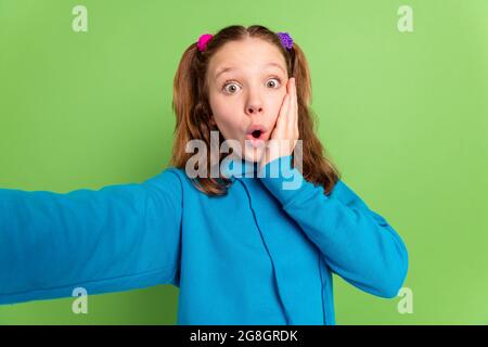 Foto di stupito scioccato giovane ragazza tenere mano guancia fotocamera rendere selfie isolato su sfondo di colore verde Foto Stock