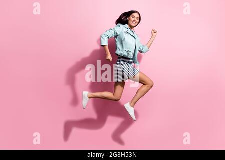 Foto a lunghezza intera di dolce bella ragazza giovane vestito giacca blu che corre saltando isolato sfondo di colore rosa Foto Stock