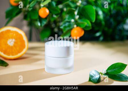 Primo piano vaso chiuso di crema idratante viso con olio essenziale di agrumi naturale e mandarino e frutti di arancio sfondo. Mockup per la cura della pelle Foto Stock