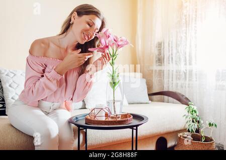 Donna che annuisce fiori di giglio rosa in vaso a casa. Young model gode bouquet di fiori freschi. Interni e decorazioni del soggiorno Foto Stock