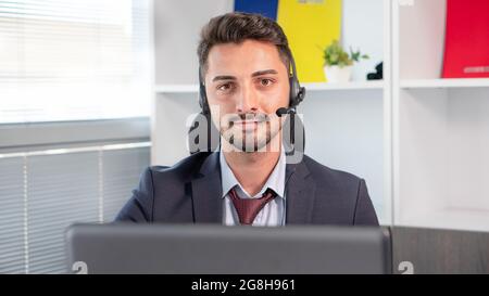 Ritratto di un uomo d'affari, un addetto del call center che indossa cuffie con microfono e lavora con un computer portatile in ufficio. Uomo in tuta consulente cliente su telefono in personalizzato Foto Stock