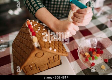 Ragazza giovane che decora una casa di pane zenzero ad un tavolo Foto Stock