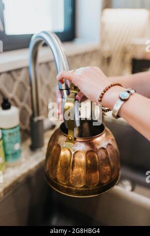 La donna fa funzionare l'acqua dal dispersore della cucina nel bollitore del tè di ottone per riscaldare Foto Stock
