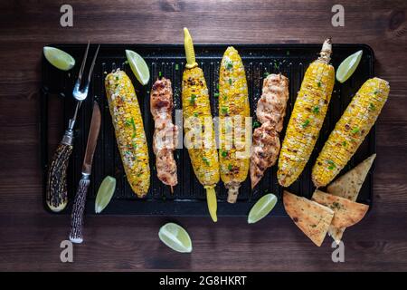 Vista dall'alto del mais alla griglia sulla pannocchia con spiedini di pollo su una padella grigliata in ghisa. Foto Stock