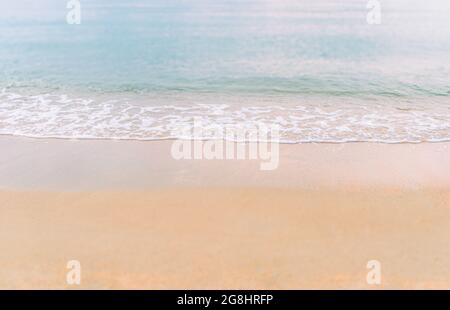 Piccola onda con le piccole bolle bianche su una spiaggia dorata al tramonto, fronte e retro sfocati, bel colore al mare. Foto Stock