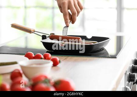 Giovane frittura gustose salsicce in cucina Foto Stock