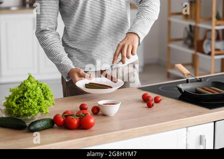 Giovane con gustose salsicce in cucina Foto Stock