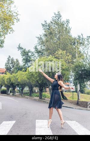 Foto verticale di ballerina latina femminile che balla su un marciapiede pedonale con costume nero e scarpe a punta Foto Stock