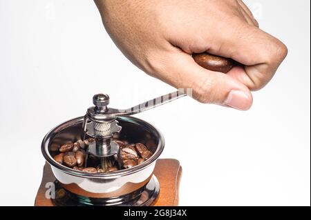 la mano di un uomo tiene la maniglia del macinacaffè per mettere a terra i chicchi di caffè tostati su sfondo bianco Foto Stock