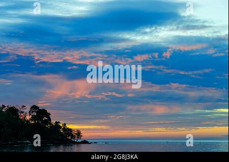 bellissimo color crepuscolo blu vivo e arance che si sono diplomate cielo e mare dietro la sagoma di una spiaggia rocciosa con alberi di cocco e pietra Foto Stock