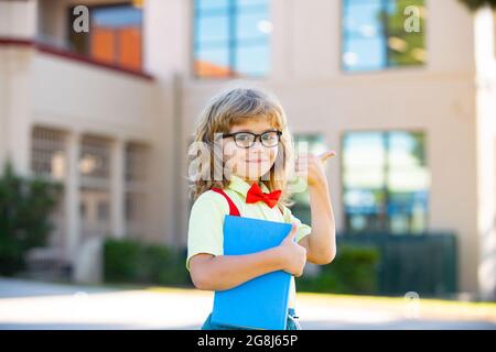 Ritorno a scuola. Bambino divertente in occhiali a scuola. Bambino della scuola elementare con libro e borsa. Educazione bambino. Foto Stock