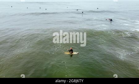 Uomo maturo remare, sdraiato su una tavola da surf - uomo sportivo senior surfing nell'oceano Pacifico, in una giornata di sole con cielo blu e onde trasparenti. Foto Stock