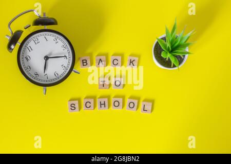 Torna a School.lettere di legno e un orologio di allarme su uno sfondo giallo, top view.The concetto dell'inizio dell'anno scolastico Foto Stock