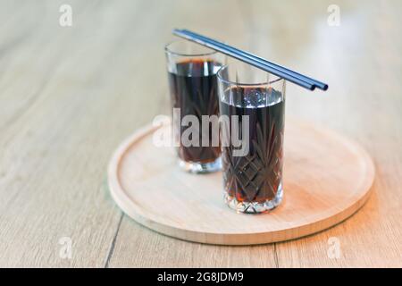 bevanda nera con cannucce. Due bicchieri Cuba Libre o cocktail a base di tè freddo a lunga isola con una cola, ghiaccio, lime, rum con cannucce su tavolo di legno con vista t Foto Stock