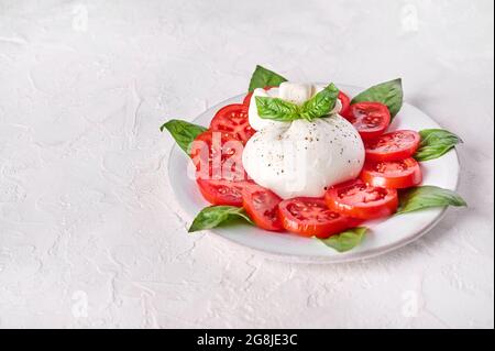 Burrata tradizionale italiana a base di panna e latte di bufalo o di mucca con basilico e pomodoro. Primo piano Foto Stock