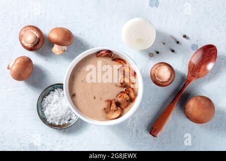 Ingredienti per zuppe di funghi. Champignons, cipolla, sale, pepe, e un cucchiaio di legno, sopra piatto colpo di posa. Semplice pasto biologico Foto Stock