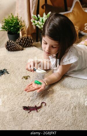 Ragazza che gioca osservando bug giocattolo con una lente di ingrandimento Foto Stock