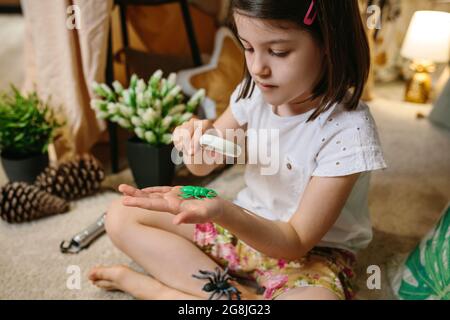 Ragazza che gioca osservando bug giocattolo con una lente di ingrandimento Foto Stock