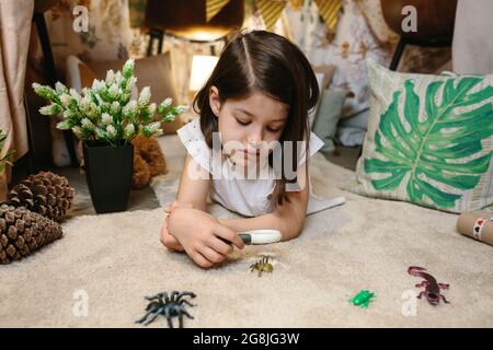 Ragazza che gioca osservando bug giocattolo con una lente di ingrandimento Foto Stock