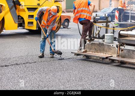 Un team di lavoratori della strada sta posando asfalto fresco con macchine stradali industriali. Foto Stock