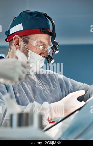Un chirurgo in duro lavoro, un medico che esegue un'operazione complessa con attrezzature moderne sulla sua testa, medicina moderna, una lotta per la vita Foto Stock
