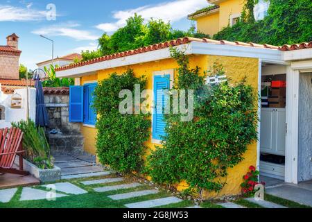 Casa tradizionale del villaggio Egeo con pareti gialle, persiane blu e edera sulle pareti. Foto Stock