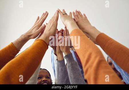 Team diversificato di persone d'affari felici alzando le braccia e unendosi le mani Foto Stock