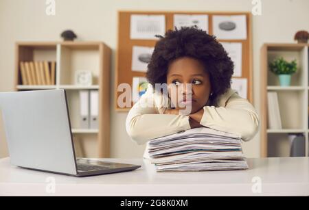 Lavoratore di ufficio femminile dalla pelle scura che ha un sacco di documenti sognando di un fine settimana o di una vacanza. Foto Stock